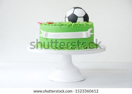 Cake on a football theme decorated with green grass and soccer ball on white background.