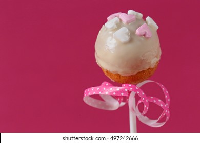Cake pop with hearts and a pink ribbon with white polka dots on a pink background 5 - Shutterstock ID 497242666
