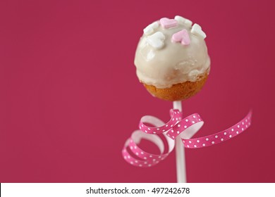 Cake pop with hearts and a pink ribbon with white polka dots on a pink background 1 - Shutterstock ID 497242678