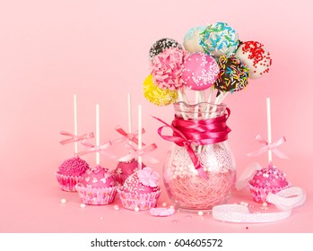 Cake pops with pink icing and decoration on paper form and colorful cake pops in glass vase on pink background - Powered by Shutterstock