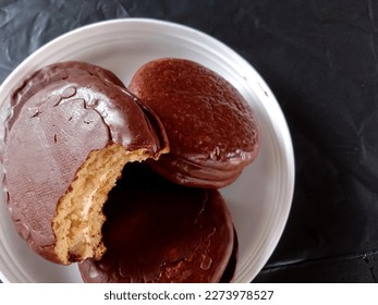 cake with two layers of brown bread cover with marshmellow filling on a white plate. photo with crumpled black background