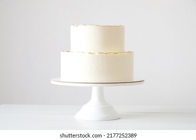 Cake with white cream, decorated with gold confectionery sprinkles on a white background. Two-tiered white wedding cake.