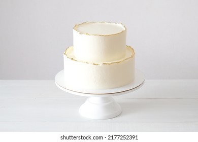Pastel con crema blanca, decorado con pasteles dorados, salpicado de un fondo blanco. Torta de bodas blanca de dos niveles.