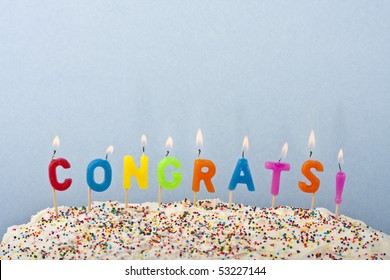 A Cake With White Frosting And Sprinkles Decorated With Candles Spelling Out Congrats