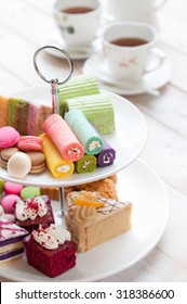 Cakes And Macaroons On Two Tiered Tray With Teapot And Cup Background. Afternoon Tea