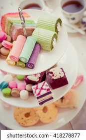 Cakes And Macaroons On Two Tiered Tray With Teapot And Cup Background. Afternoon Tea