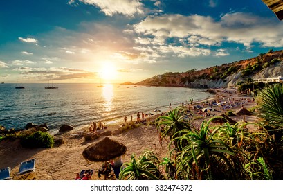 Cala dHort Beach at sunset. People sunbathing, have a party on the sandy tropical picturesque rocky beach during sunset. This beach is very popular for clubbers and vacationers Balearic Islands. Ibiza