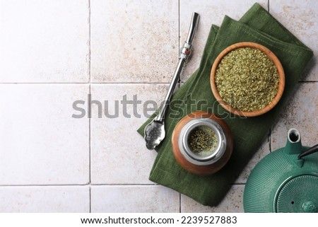 Calabash, bombilla, bowl of mate tea leaves and teapot on tiled table, flat lay. Space for text