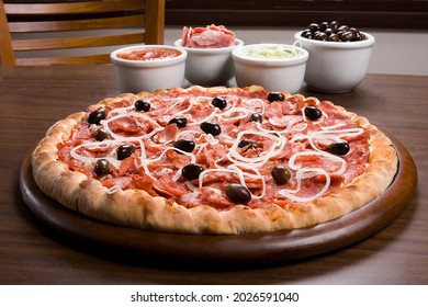 Calabrian sausage pizza, typical Brazilian pizza, on wooden board over table background, pizza ingredients make up the backdrop. - Powered by Shutterstock