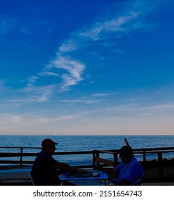 Calahonda, Malaga, Spain; 04-30-2022: Two Men Playing Cards In A Pleasant Evening By The Mediterranean Sea At Sunset