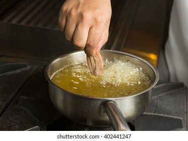 Calamari ring being placed into a pan of hot bubbling oil. - Shutterstock ID 402441247