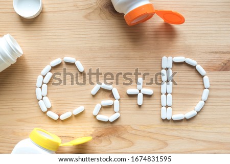 Calcium and Vitamin D Generic Tablets. White pills forming shape to Ca+D alphabet on wooden background, copy space, top view.