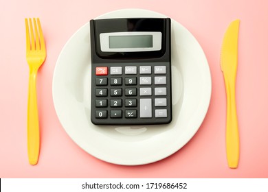 Calculate Expensive Food Spending Costs, Counting Calories And Weight Loss Program Concept With Calculator Onn Empty Plate, Yellow Fork And Knife Isolated On Pink Background