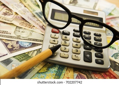 Calculating Numbers For Income Tax Return With Glasses Pen And Calculator.  Notes And Bills Of Different States. International Banknotes. Wooden Pen On Various Money Bill