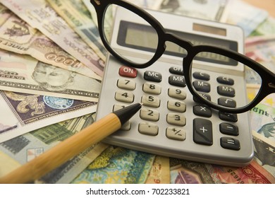 Calculating Numbers For Income Tax Return With Glasses Pen And Calculator.  Notes And Bills Of Different States. International Banknotes. Wooden Pen On Various Money Bill