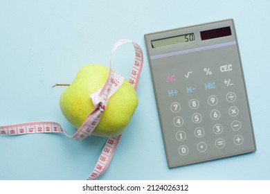 Calculator and apple with measuring tape on blue background. Weight loss, counting calories and healthy eating concept - calculate daily nutrition intake. Top view.