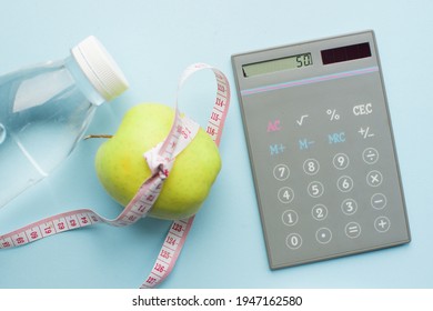 Calculator, bottle of water, apple with measuring tape on blue background. Weight loss, counting calories and healthy eating concept - calculate daily nutrition intake. Top view.