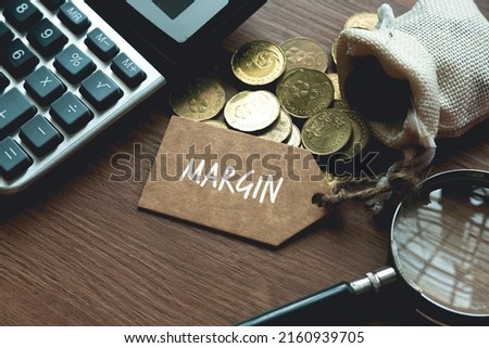 A calculator, magnifying glass, coins and tag written with Margin. Business and finance concept.