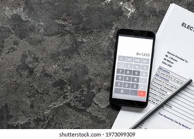 Calculator mobile application on screen of phone and documents on dark background