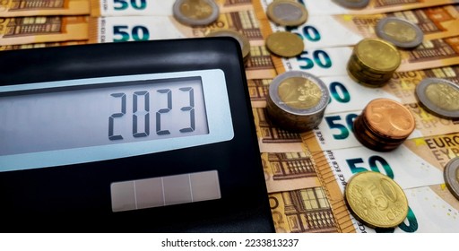 Calculator on the background of euro bills and coins. On the calculator screen, the number 2023. Fiscal year 2023