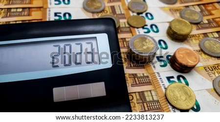 Calculator on the background of euro bills and coins. On the calculator screen, the number 2023. Fiscal year 2023