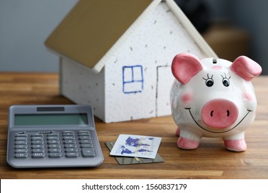 Calculator With Piggy Bank Against Home Background Closeup. Mortage Credit Concept