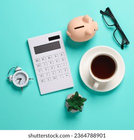 Calculator, piggy bank, alarm clock, pen, coffee cup, eyeglasses and plant on blue background. Business concept. Workspace. Top view. Flat lay. - Shutterstock ID 2364788901