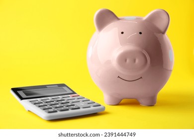 Calculator and pink piggy bank on yellow background, closeup