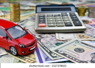 Calculator and red toy car on a variety of national currency banknotes background.  Concept of the cost of purchasing, renting and maintaining a car - image