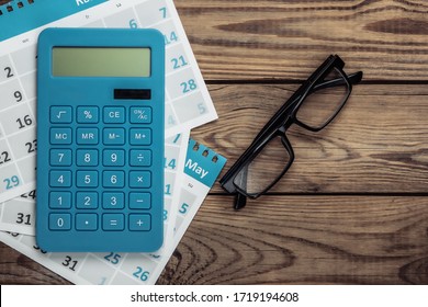 Calculadora com folhas do calendário mensal, óculos em fundo de madeira. Cálculo econômico, custeio. Vista superior