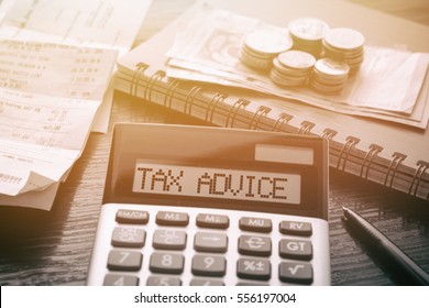 Calculator with text Tax Advice. Calculator, currency, book, bills and pen on wooden table. Business, finance conceptual. 