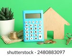 Calculator, wooden house, keys, houseplant and money on green background, closeup. Mortgage concept