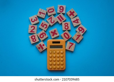 Calculator and a wooden number and mathematical symbol on blue background.