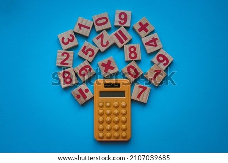 Calculator and a wooden number and mathematical symbol on blue background.