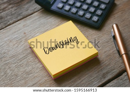 Calculator,pen and yellow sticky notes written with Downsizing on wooden background.