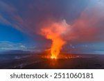 The caldera, or crater, on Kilauea in Hawaii shows boiling lava and steam rising into the dark sky at night and blue hour