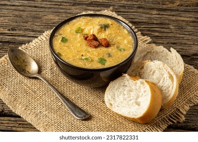 Caldo de Kenga Cassava broth with shredded chicken, typical Brazilian food known as (Caldo de Quenga), in a black pot on top of a rustica with a spoon and slices of bread,  with selective focus - Shutterstock ID 2317822331