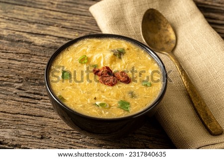 Caldo de Kenga Cassava broth with shredded chicken, typical Brazilian food known as (Caldo de Quenga), in a black pot on top of a rustica with a spoon and slices of bread,  with selective focus