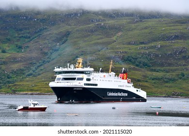 Caledonian McBrayne Ferry entering Ullapool Harbour with low mist in background and small red fishing boat. Ullapool, Ross and Cromarty, Scotland UK. aUGUST 2021