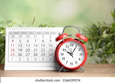 Calendar and alarm clock on wooden table against blurred green background