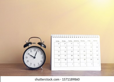 Calendar and alarm clock on wooden table against beige background