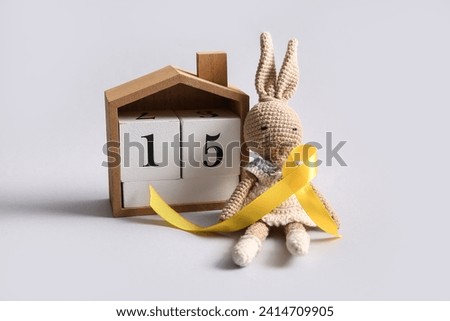 Calendar with date of Childhood cancer awareness day, bunny toy and golden ribbon on white background