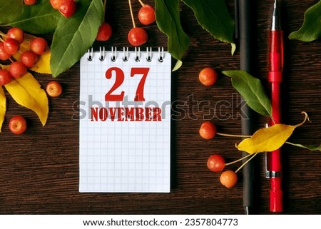 calendar date on wooden dark desktop background with autumn leaves and small apples. November 27 is the twenty-seventh day of the month.