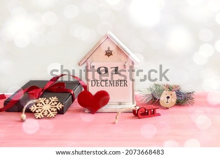 Calendar for December 1: decorative house with the name of the month in English, number 01, gift wrapped, tied with a red ribbon, red heart, New Year's toys, bokeh.