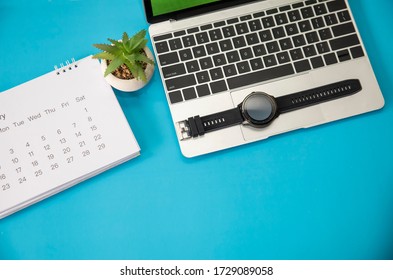 Calendar And Laptop For Planner To Plan Reminder Daily Appointment Timetable, Organization And Meeting Agenda Of Job On Blue Desk, Work Online At Home. Cactus, Watch Clock Place On Table.