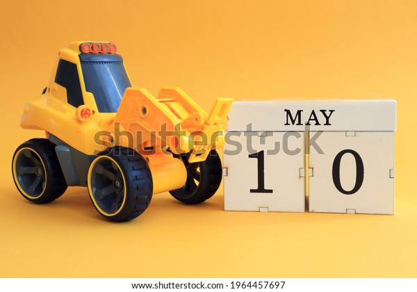 Calendar for May 10: toy yellow tractor with\
the number 10 on the cube, the name of the month in English on a\
yellow background