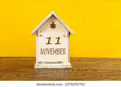 Calendar for November 11: the name November in English, numbers 11 on a decorative house on a wooden table, yellow background