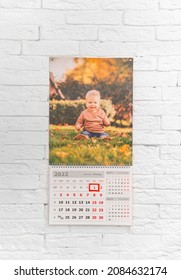 Calendar With A Photo Of Child In Front Of White Brick Wall. Printed Products With An Image. A Gift To Parents And Grandparents From Children And Grandchildren For New Year. Services Of Photographer.