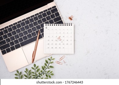Calendar with rose gold pen on laptop on white quartz background with copy space, flat lay