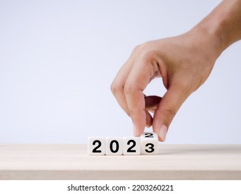 The Calendar Year 2022 Changed To 2023, Success Concept. White Cube Blocks Turning By Hand For The Transition From 2022 To 2023, Preparation For Merry Christmas And Happy New Year On Blue Background.